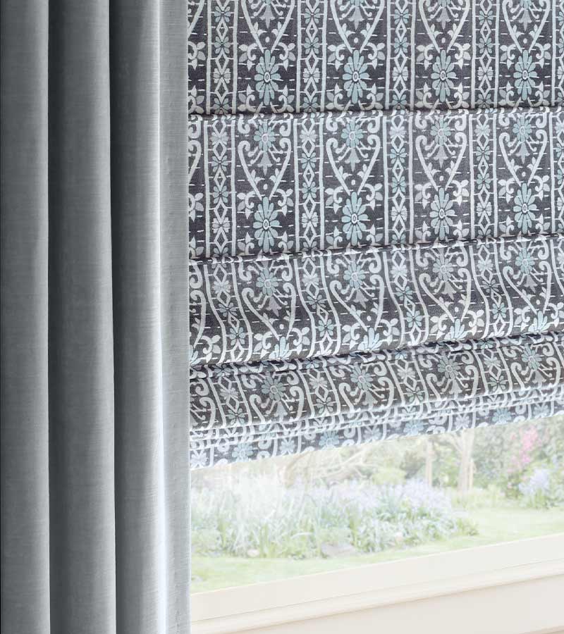 plush blue drapes framing blue and gray and white patterned roman shades